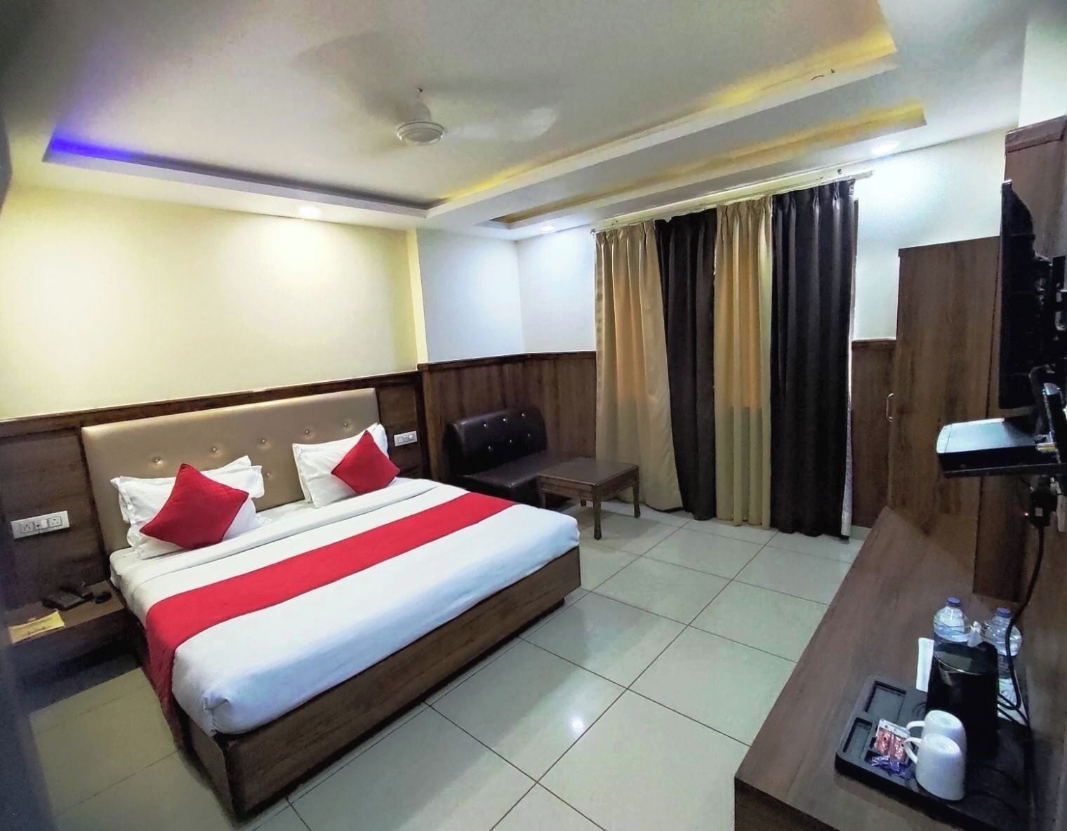 Una habitación de hotel con cama, escritorio, silla, televisor y cortinas.