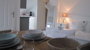 A dining area with a wooden table set for a meal, a kitchen in the background, and a bedroom with a bed and nightstand. - Haus Grünewald Unsleben (Unsleben)
