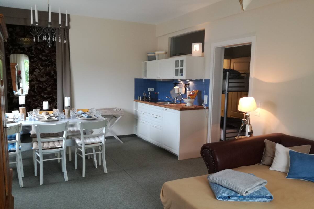 Ein kleines Hotelzimmer mit Essbereich, Küchenzeile und einem Bett mit blauem Kopfkissen.