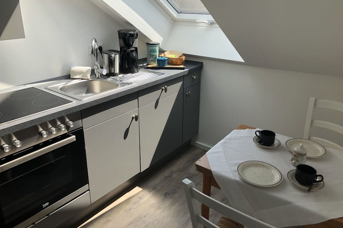 Eine kleine Küche mit Dachfenster, einer Kaffeemaschine und einem Esstisch für zwei Personen.