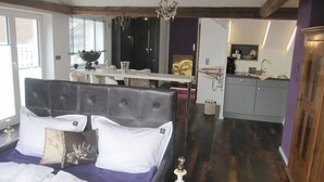 A bedroom with a large bed, a small table, and a view of a kitchen and bathroom. - Haus Grünewald Unsleben (Unsleben)