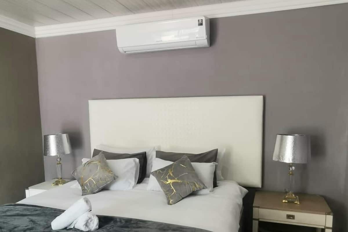 A neatly made bed with a white headboard, two bedside tables with lamps, and a wall-mounted air conditioner.