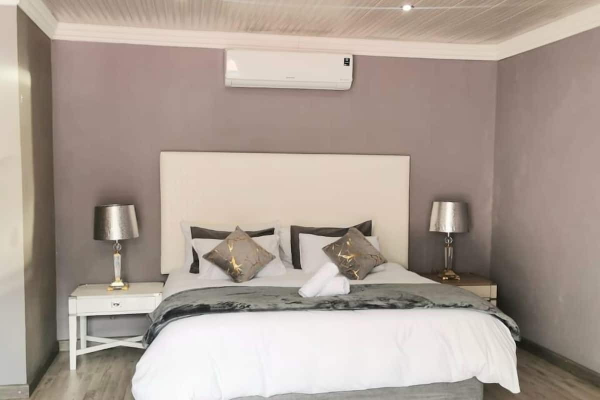 A bedroom with a bed, two bedside tables, a wall-mounted air conditioner, and a ceiling with a ribbed design.