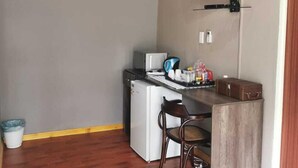 A compact kitchen with a built-in microwave, a small refrigerator, and a wooden dining table with a chair. A flat-screen TV is mounted on the wall above the counter. - Botle Ba Afrika Lodge (Vereeniging)