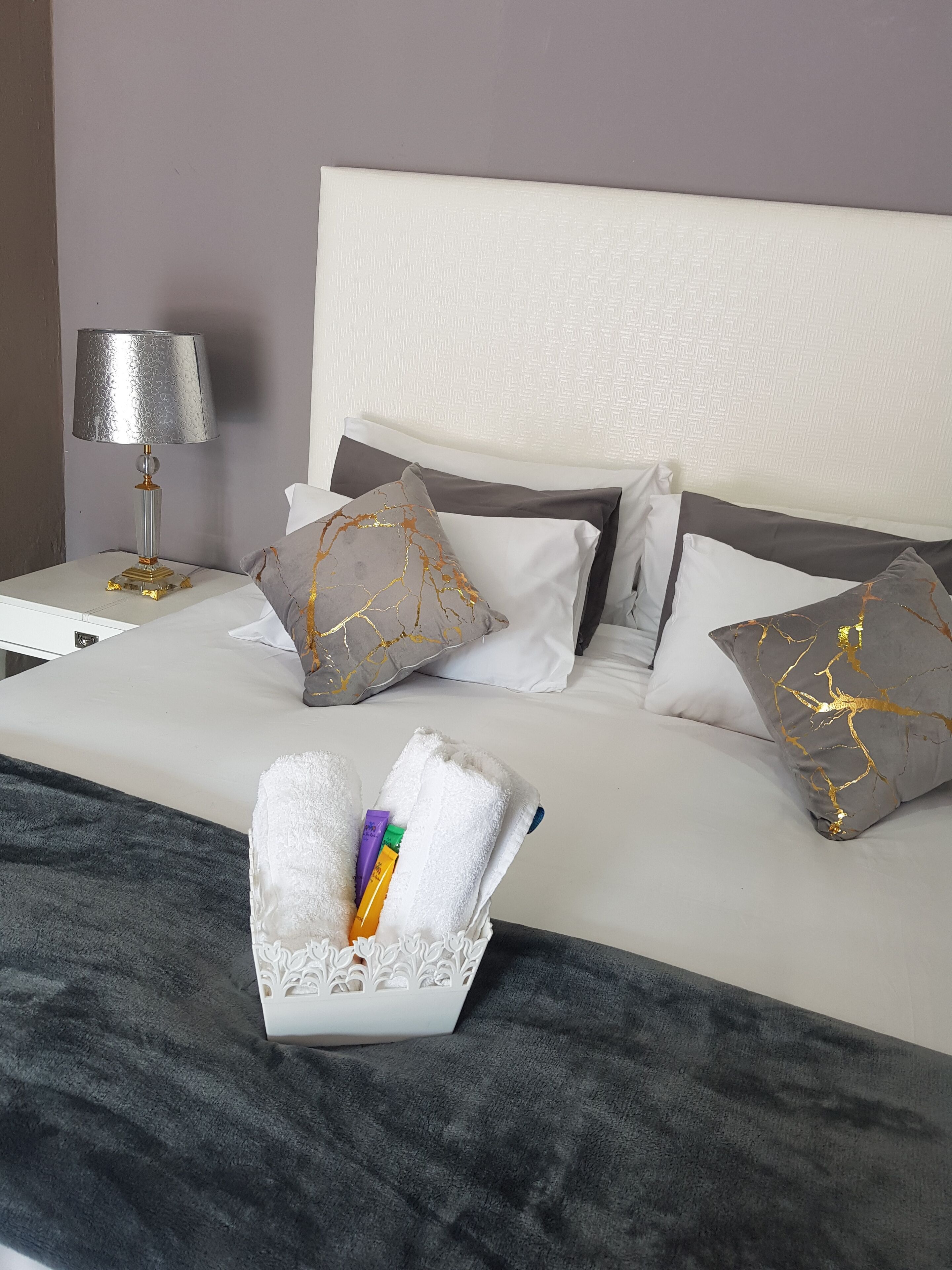 A neatly made bed with white and grey pillows, a grey throw blanket, and a white decorative box with toiletries.