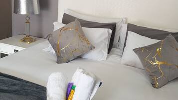A neatly made bed with white and grey pillows, a grey throw blanket, and a white decorative box with toiletries.