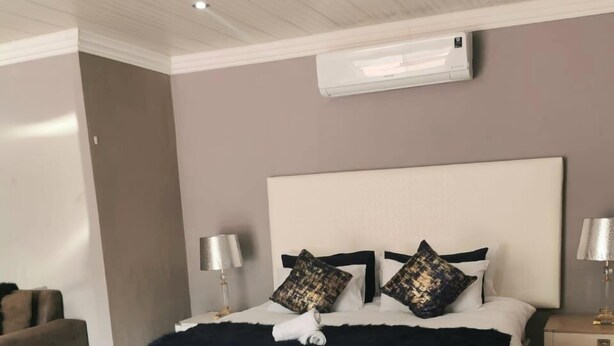 A modern bedroom with a large bed, two bedside tables, and an air conditioning unit on the wall. - Botle Ba Afrika Lodge (Vereeniging)