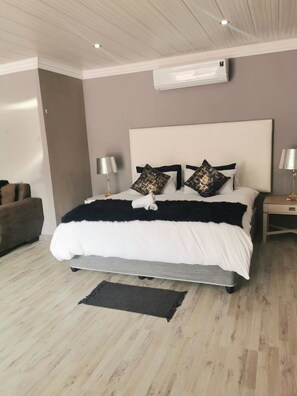 Un dormitorio moderno con una cama grande, cabecera, lámparas de noche y una lámpara de pie.