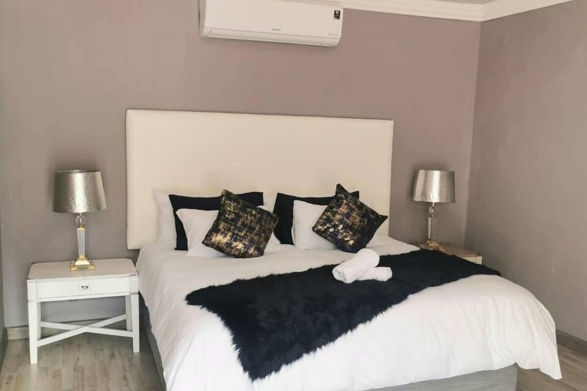 A bedroom with a bed, two nightstands, a ceiling fan, and an air conditioning unit.