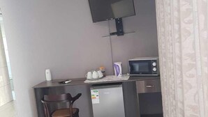 A compact kitchenette with a microwave, refrigerator, and a small table with a chair. A television is mounted on the wall above the table. - Botle Ba Afrika Lodge (Vereeniging)
