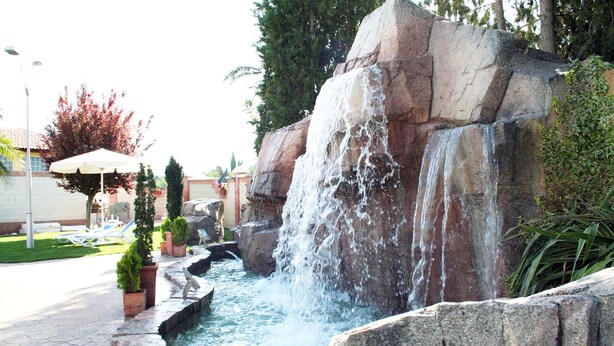 A landscaped area with a waterfall feature, stone steps, and a pool. - Hotel Juleca (Jaén)