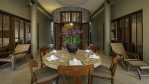 Een ronde eettafel met stoelen, een bloemstuk in het midden en een accentmuur van steen.