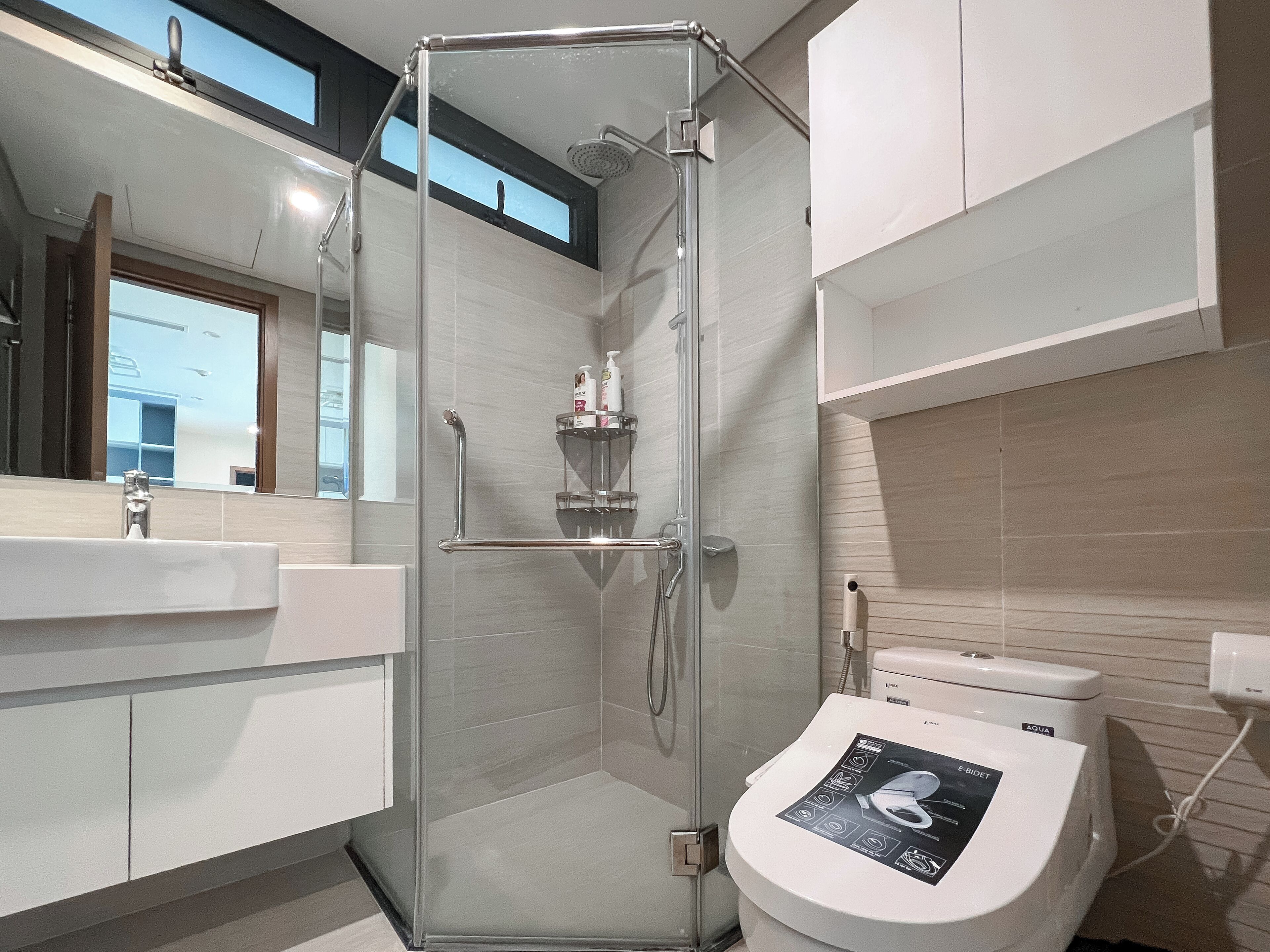 Une salle de bain moderne avec une douche à parois de verre, des toilettes blanches et un lavabo avec un miroir au-dessus.