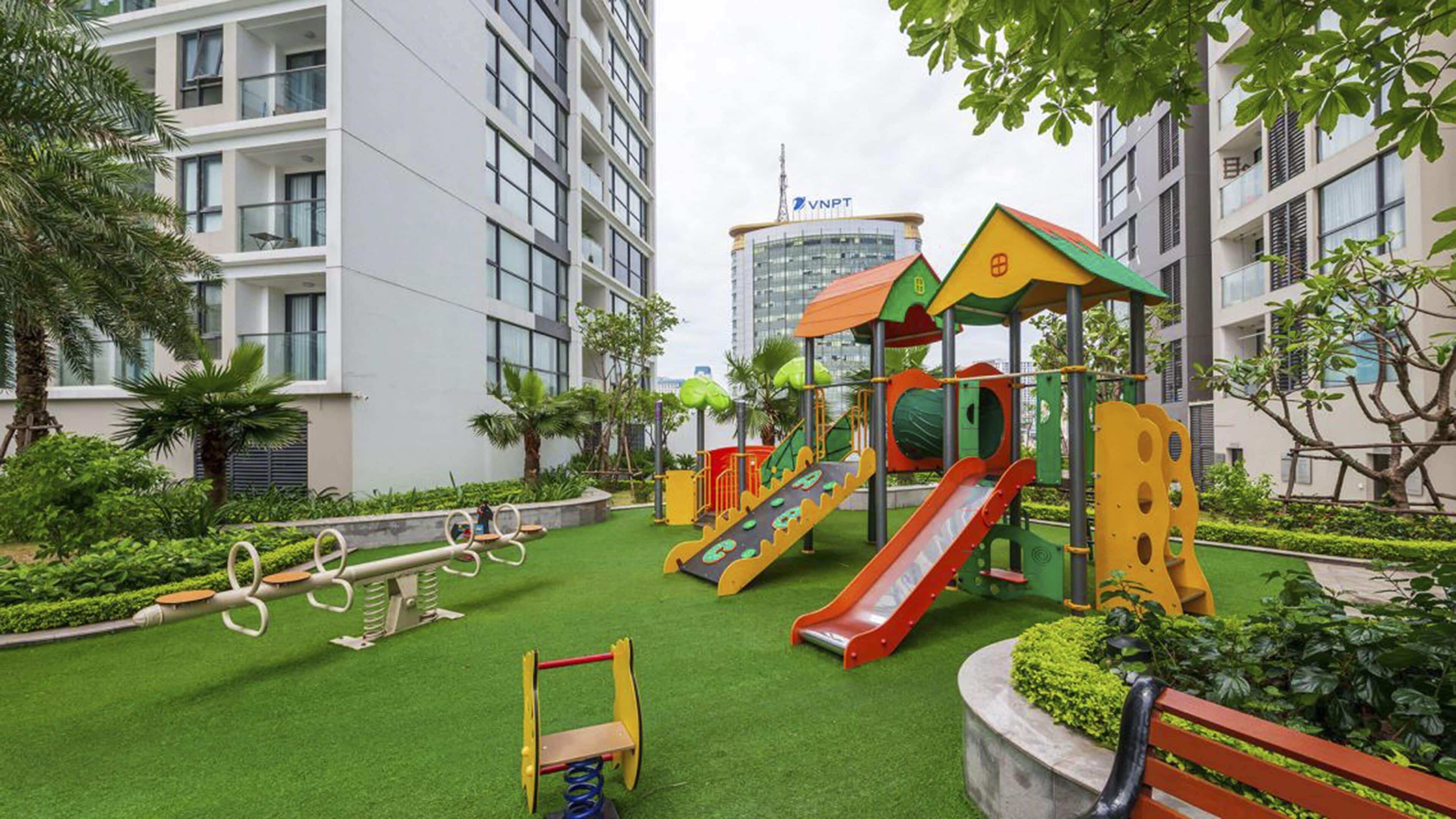 A playground with slides and swings, surrounded by greenery and modern buildings.