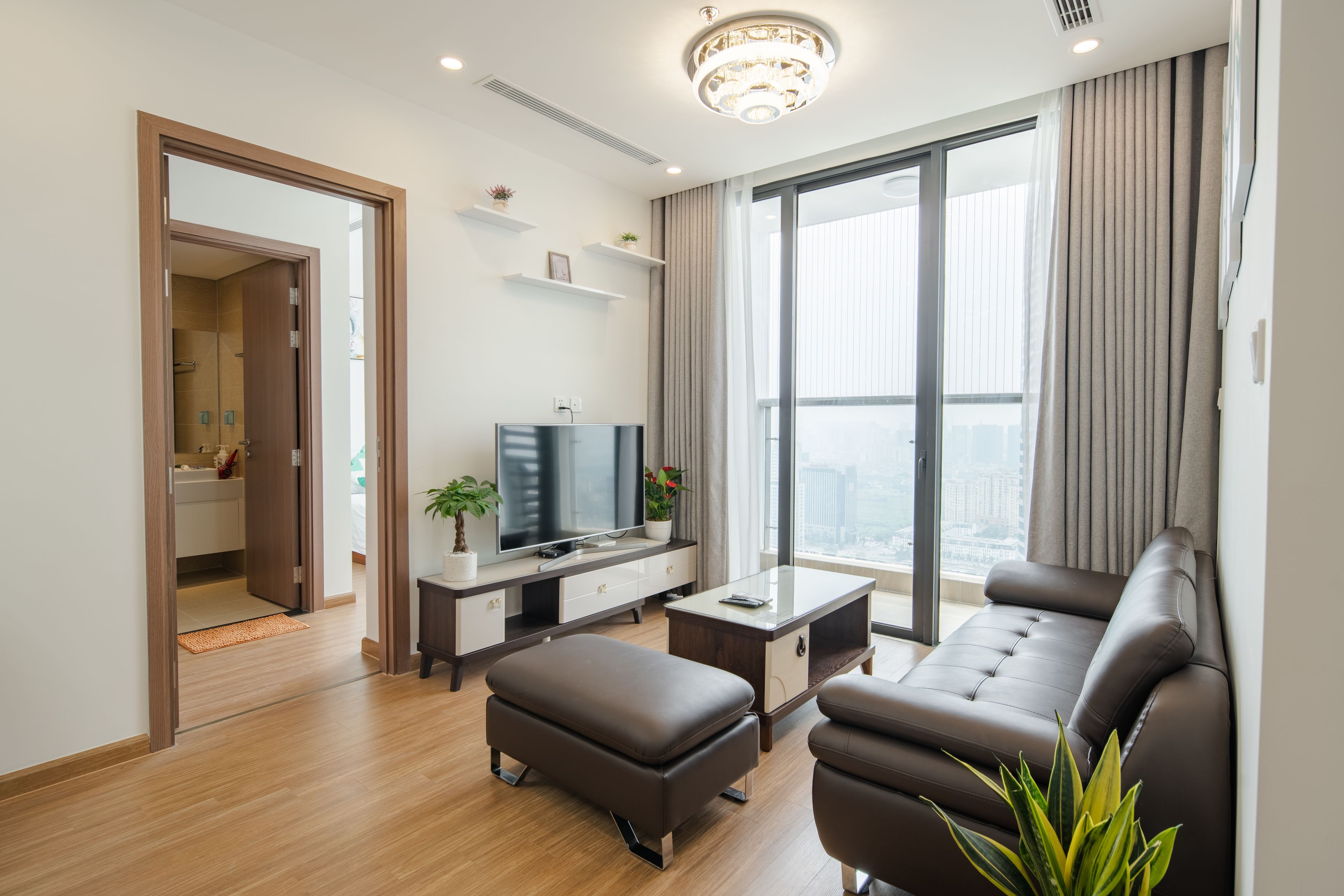 A modern living room with a sofa, ottoman, TV, and a large window with curtains.