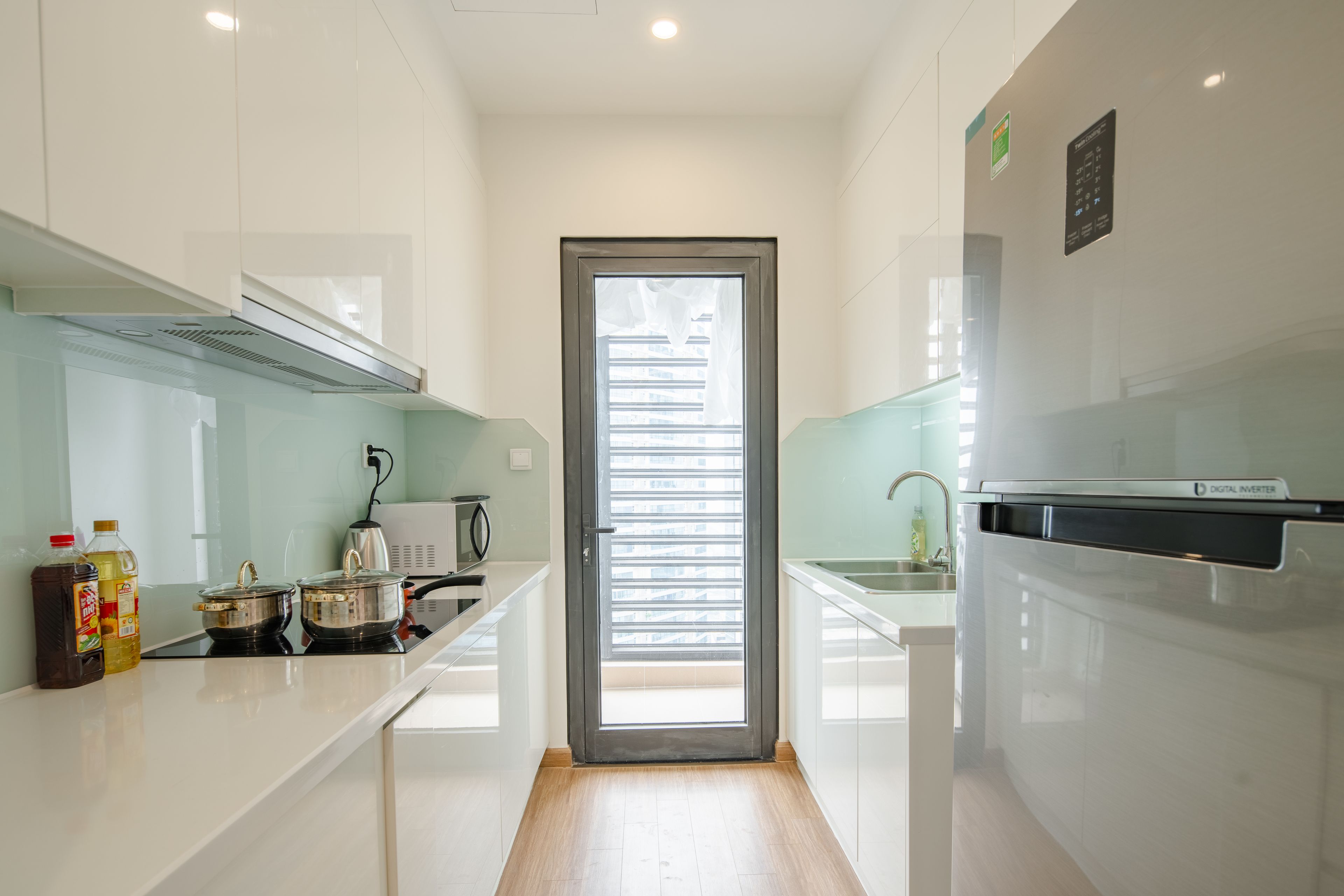 Une cuisine moderne avec des meubles blancs, une cuisinière à induction numérique et une vue sur l’extérieur par une porte.