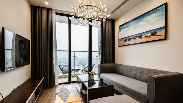 Una sala de estar moderna con un sofá, una mesa de centro de vidrio, un televisor de pantalla plana y un cuadro de barcos en la pared.