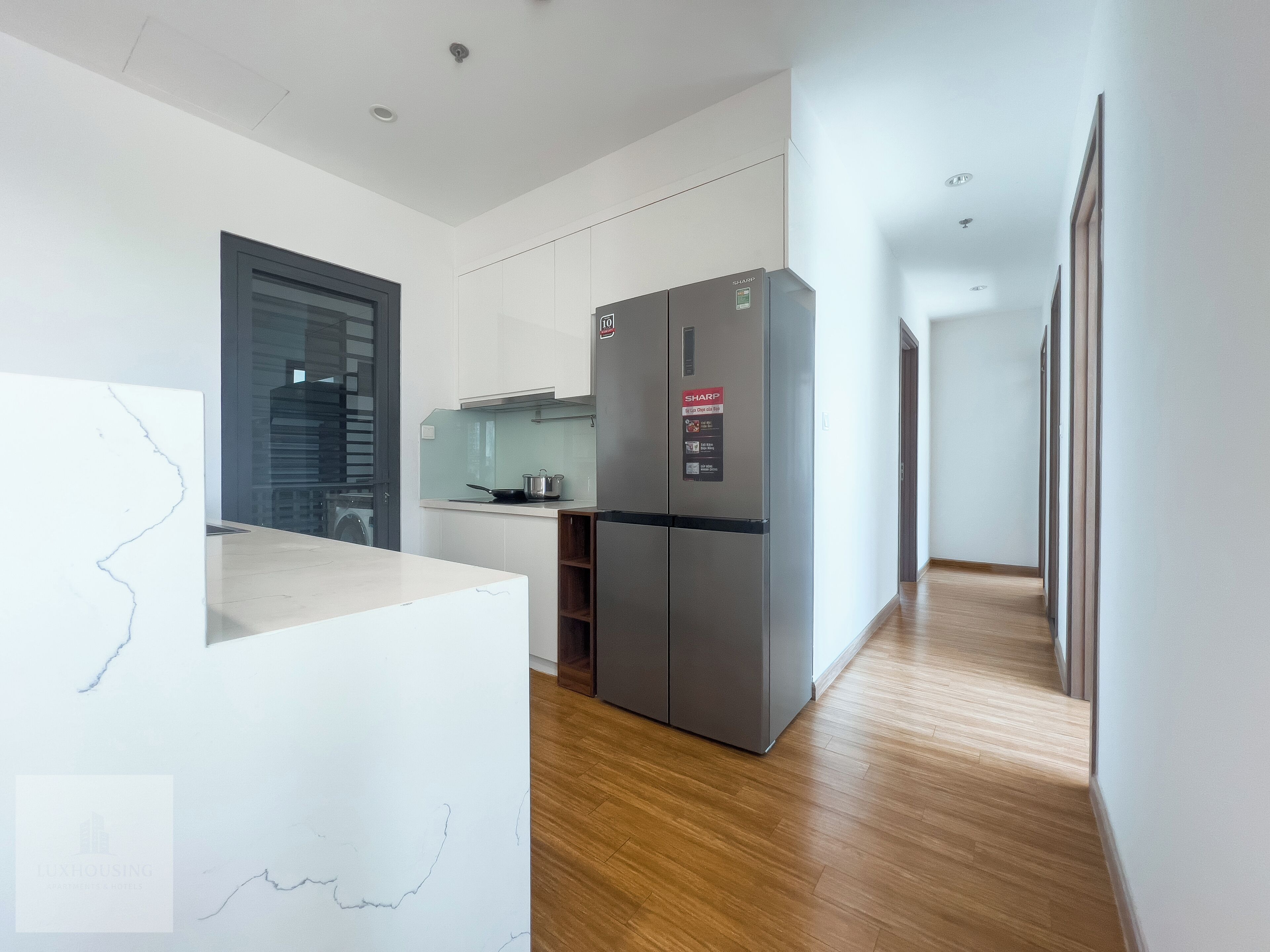 Une cuisine moderne avec des meubles blancs, un réfrigérateur en acier inoxydable et un plancher en bois.