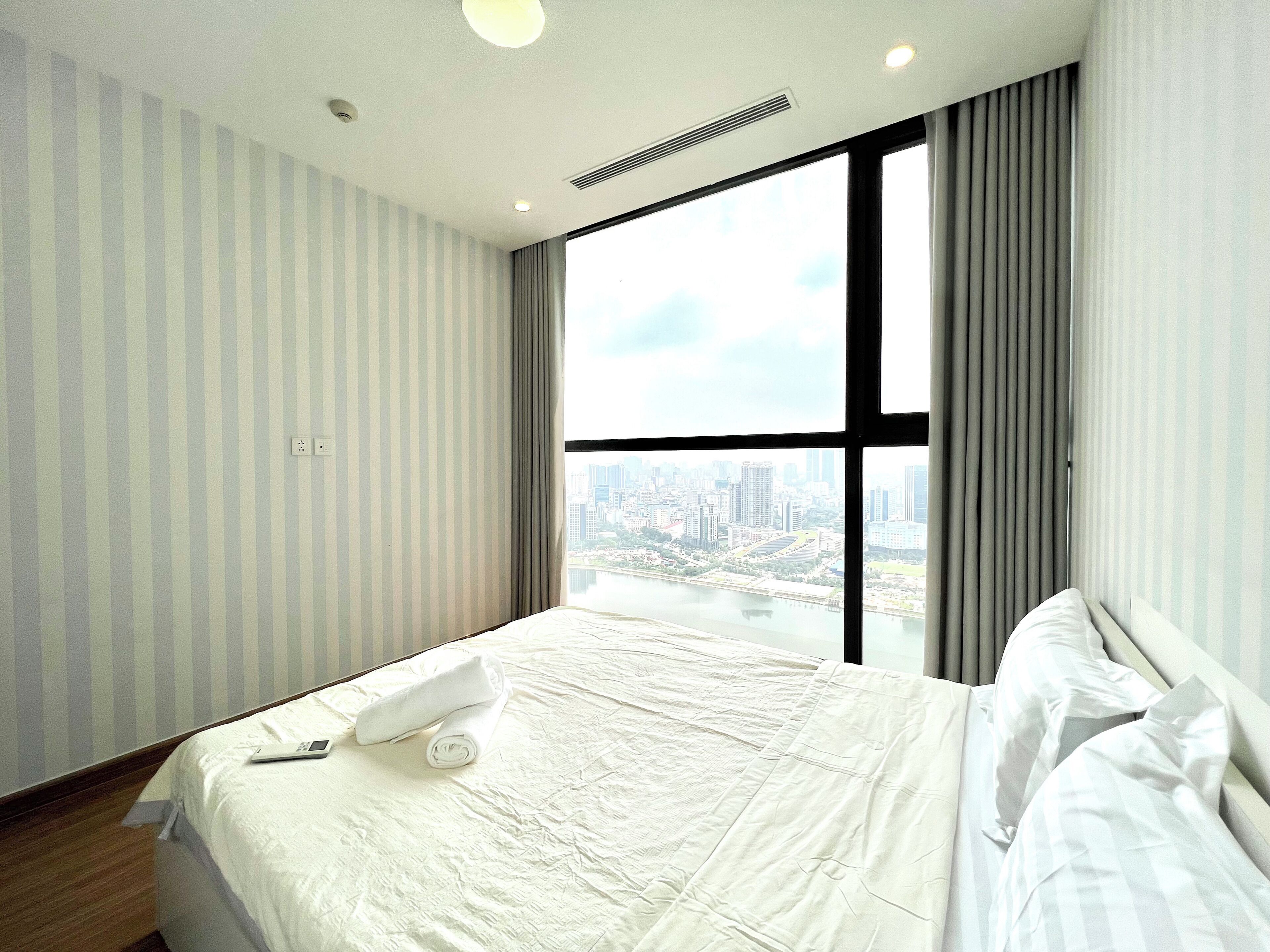 Een hotelkamer met een groot raam, een bed met witte lakens en uitzicht op een stadsbeeld.