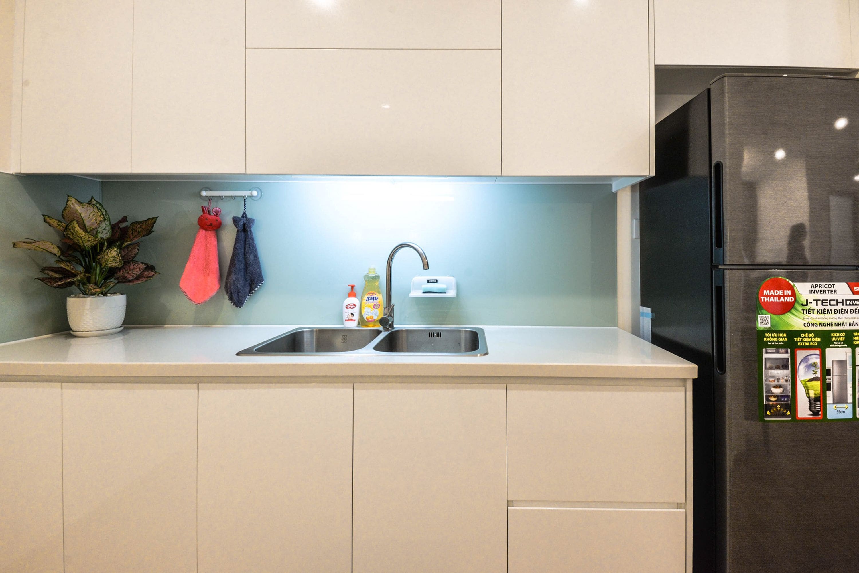 A kitchen with two sinks, a potted plant, and a refrigerator.