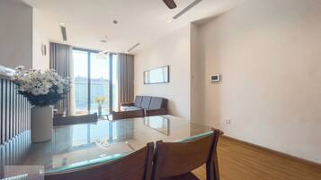 A modern hotel room with a glass dining table, a sofa, and a ceiling fan.