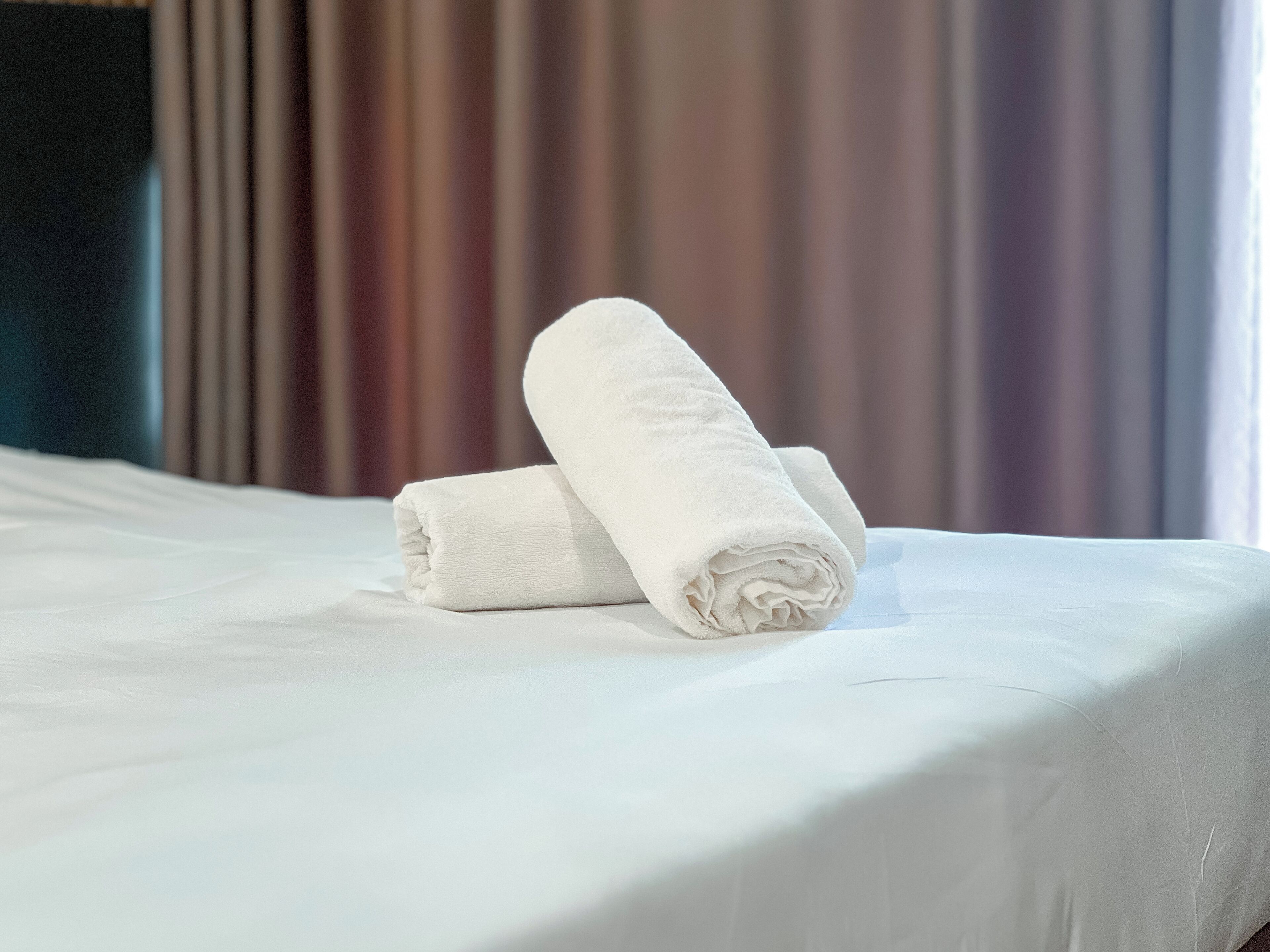 Een net opgemaakt bed met twee opgerolde witte handdoeken.