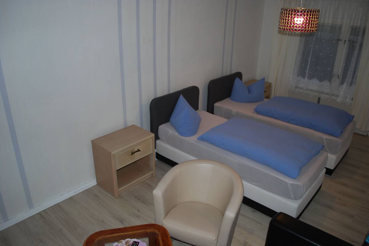 A bedroom with two beds, a chair, a nightstand, and a hanging lamp.