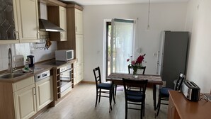 A compact kitchen with wooden cabinets, a microwave, an oven, and a dining table with chairs. - Pension Scheffler (Potsdam)
