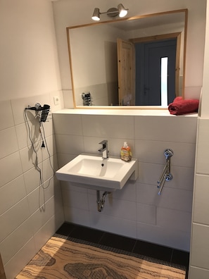 Un baño con un lavamanos blanco, un espejo encima y un perchero con una toalla roja.