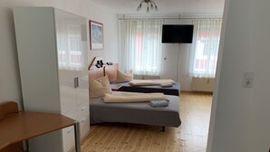 A modern bedroom with two beds, a desk, a TV, and a window with curtains. - Pension Scheffler (Potsdam)