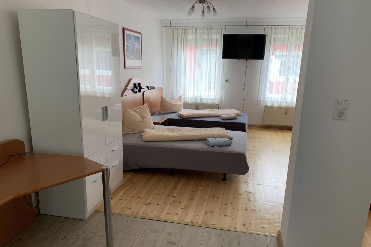 A modern bedroom with two beds, a desk, a TV, and a window with curtains.