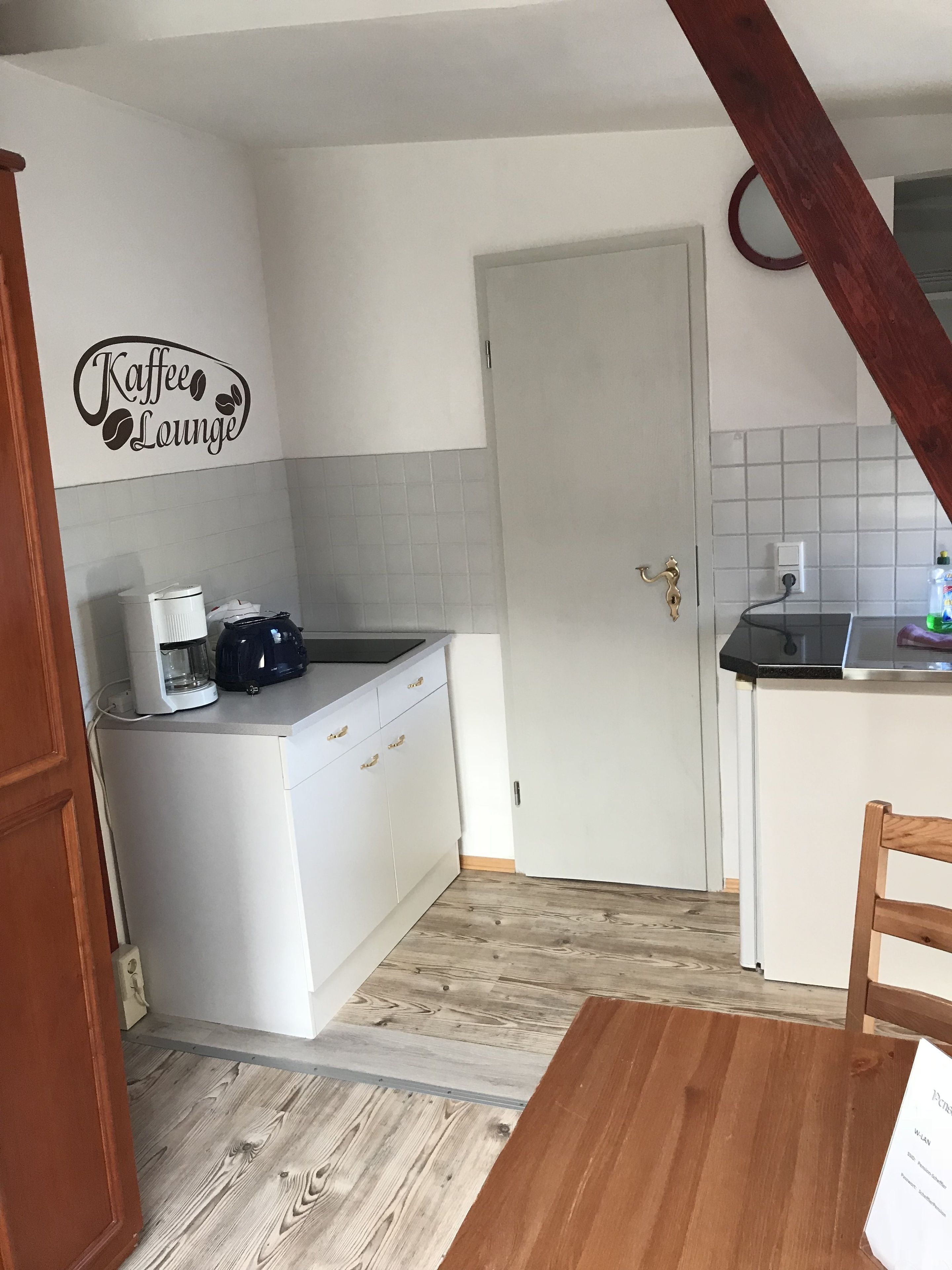 A compact kitchen with a coffee machine, a white cabinet, and a door.