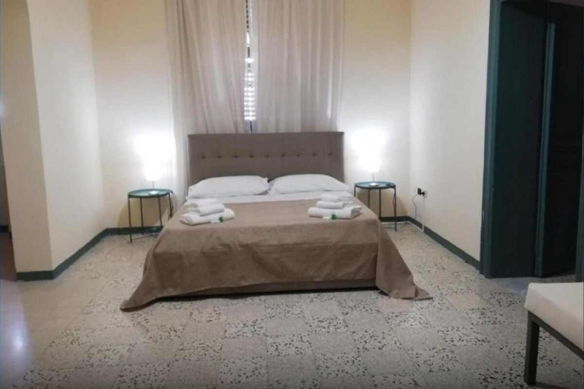 A neatly made bed with a brown bedspread and white pillows, two bedside tables with lamps, and a door to the right.