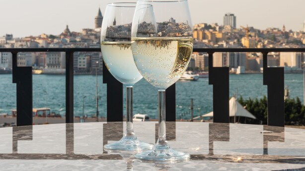 Två glas vitt vin står på ett bord med en stadsbild i bakgrunden.