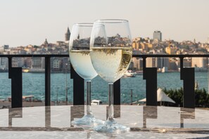 Dos copas de vino blanco sobre una mesa, con vista a un paisaje urbano al fondo.