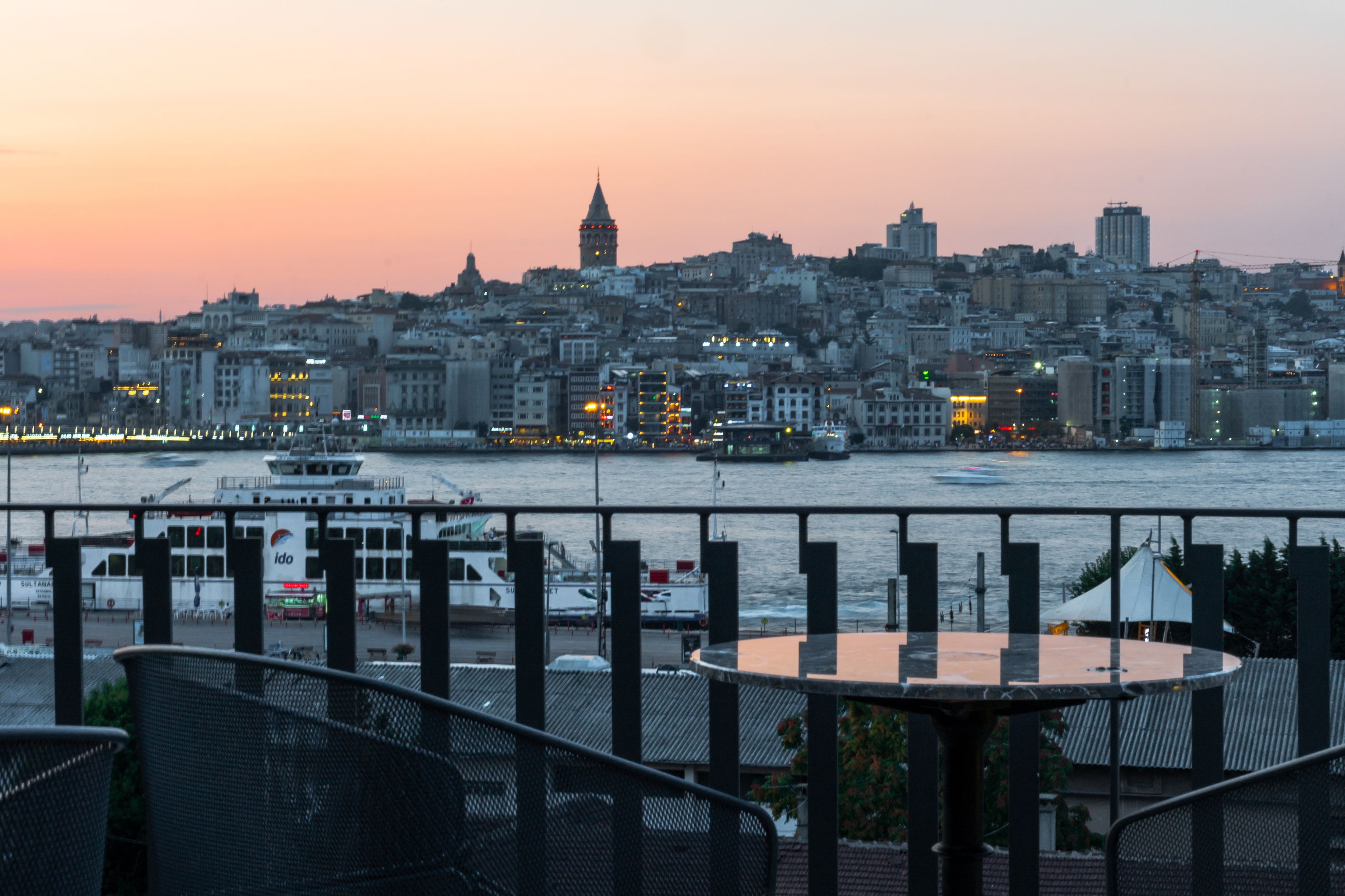 Un paisaje urbano al atardecer con vista al paseo marítimo, que incluye barcos y un ferry.