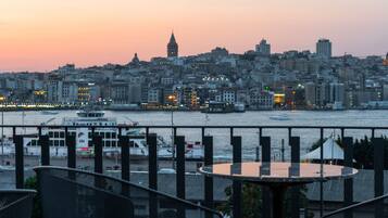 Un paisaje urbano al atardecer con vista al paseo marítimo, que incluye barcos y un ferry.