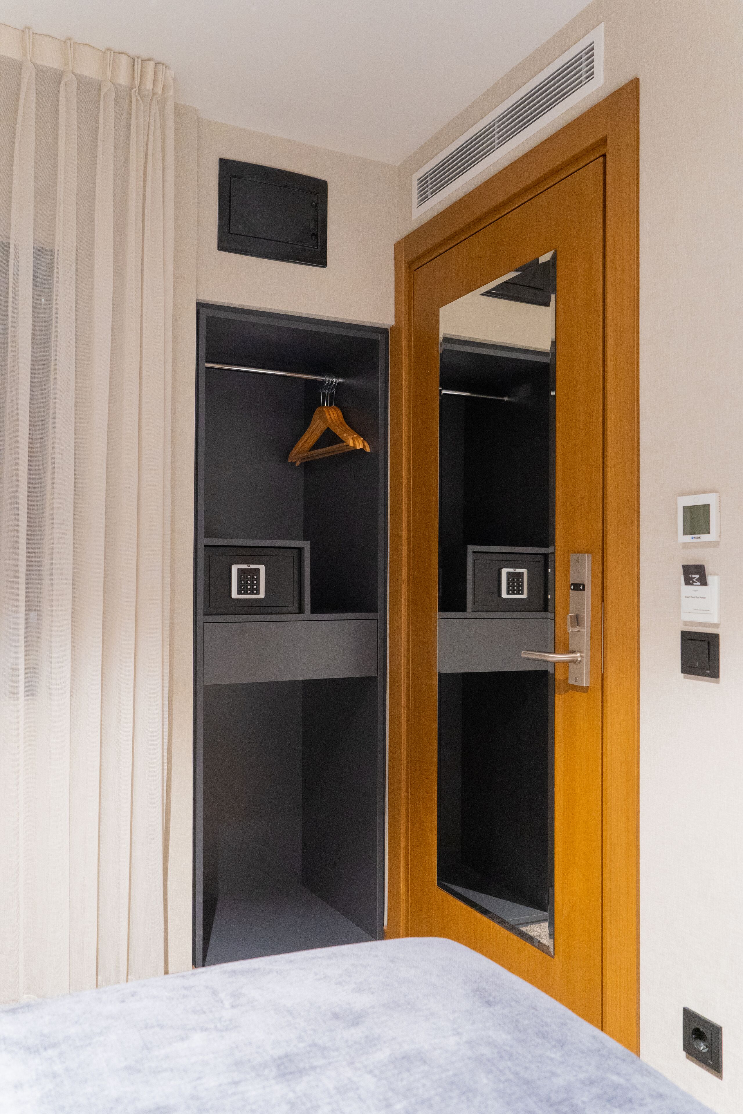 Une chambre d’hôtel avec une porte en bois, un miroir, un porte-manteau et un petit coffre-fort.