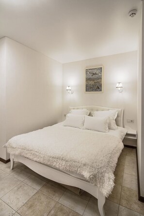 A bedroom with a large bed, two bedside lamps, a framed artwork on the wall, and a white fluffy throw blanket. - Apart Hotel Quartet (Odesa)