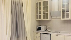A compact kitchen with a microwave, a small refrigerator, and a sink. There are cabinets above the counter and a window with sheer curtains. - Apart Hotel Quartet (Odesa)