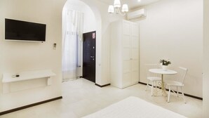 A modern hotel room with a flat-screen TV, a small seating area with a table and chairs, a wardrobe, and a large window with curtains. - Apart Hotel Quartet (Odesa)