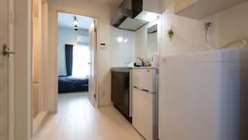 Um corredor estreito que leva a um quarto com uma cama e uma janela. Uma cozinha compacta com geladeira, pia e fogão pode ser vista.