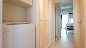 A laundry area with a washing machine and a dryer, a sliding door leading to a bedroom with a bunk bed, and a visible power outlet. - MP HOTELS Nagasaki Mizubenomori (Nagasaki)