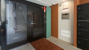 A hotel entrance with a black door, a red emergency exit sign, a green door, and a wall-mounted elevator control panel. - MP HOTELS Nagasaki Mizubenomori (Nagasaki)