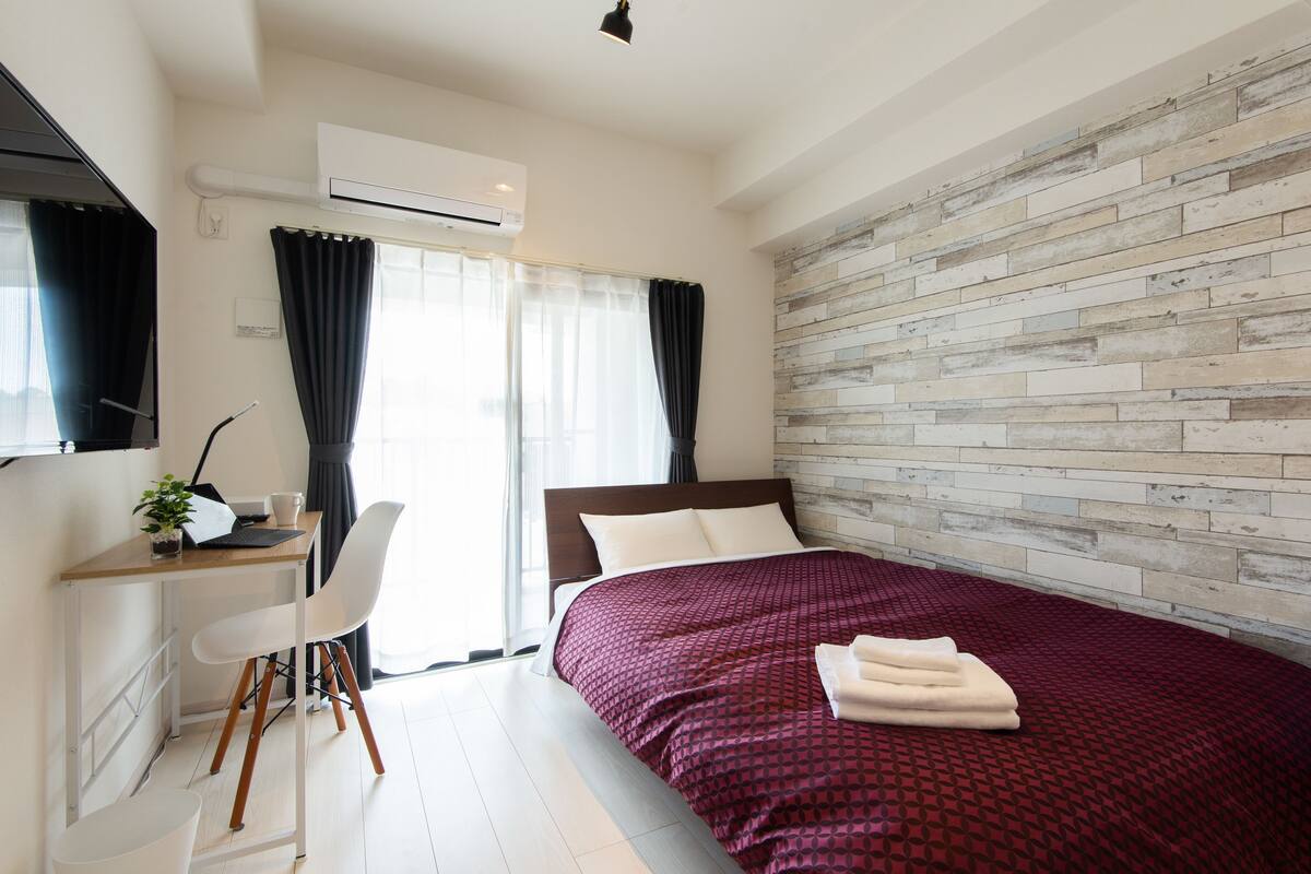 Habitació d'hotel moderna amb una paret d'accent de fusta, un llit gran amb colcha vermella amb dibuixos, un escriptori amb un ordinador portàtil i una cadira blanca.