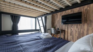 A modern hotel room with a wooden ceiling, a large bed with a patterned duvet, a flat-screen TV mounted on the wall, and a small desk with a chair. - MP HOTELS Nagasaki Mizubenomori (Nagasaki)