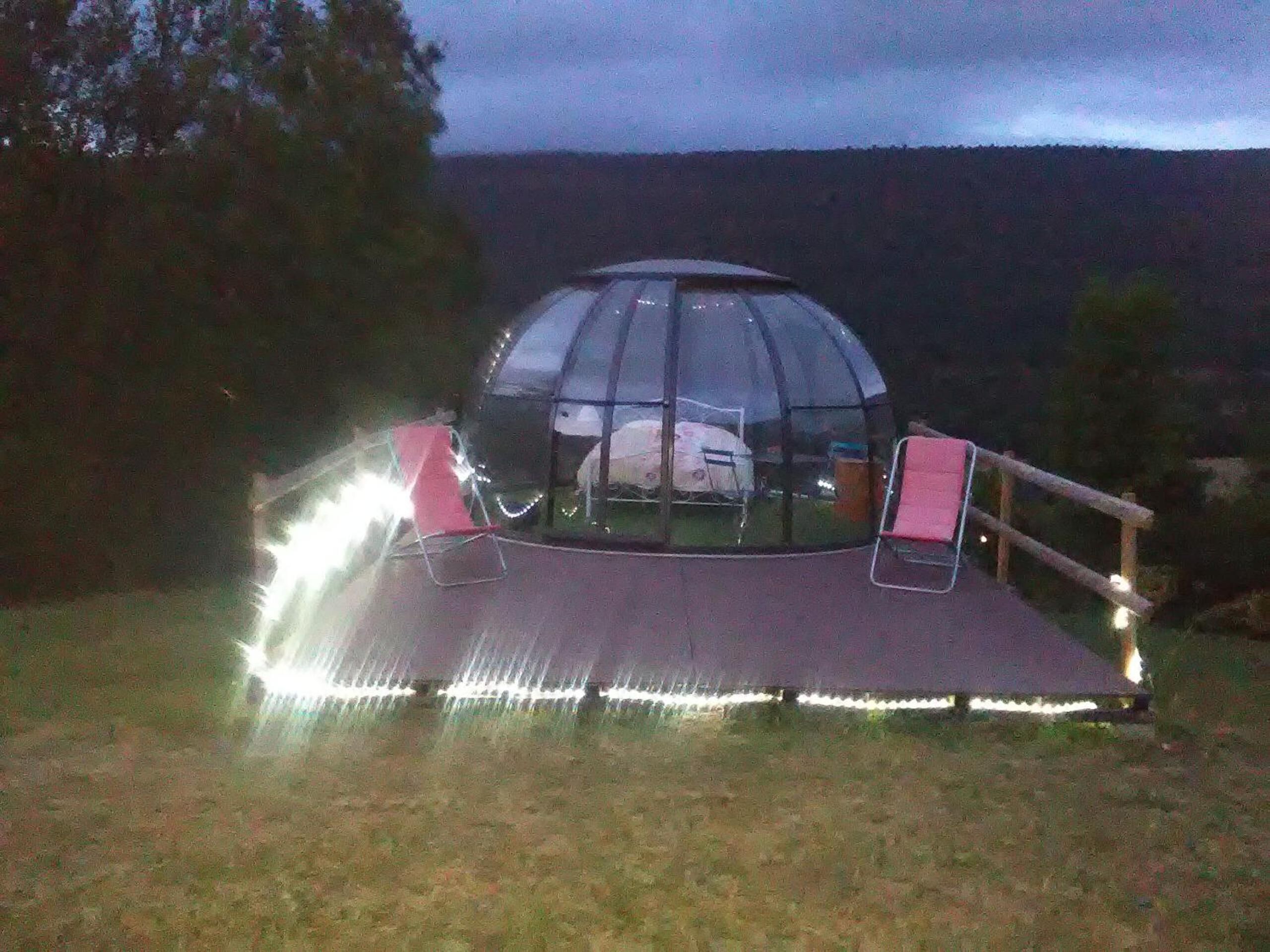 A dome-shaped tent with a flat roof, surrounded by a wooden deck with railings, and a small table with chairs inside.