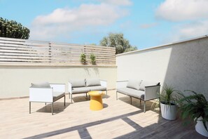 Une terrasse sur le toit avec deux canapés blancs, une table basse jaune et des plantes en pot.