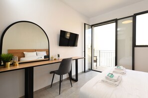 A modern hotel room with a bed, a desk with a chair, a flat-screen TV, a large mirror, and a balcony with a glass door.