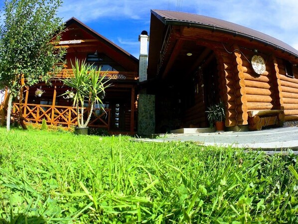 A log cabin with a wooden exterior, a porch with a railing, and a chimney.